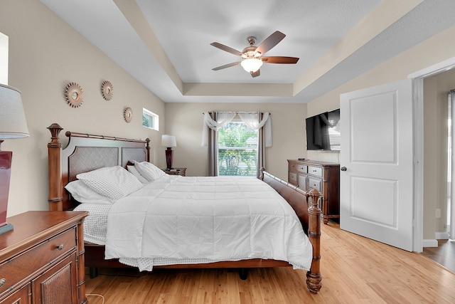 bedroom featuring ceiling fan, a raised ceiling, and light hardwood / wood-style floors