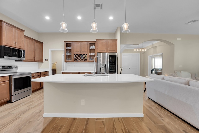 kitchen featuring light hardwood / wood-style flooring, backsplash, an island with sink, sink, and stainless steel appliances