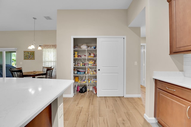 kitchen with a notable chandelier, light wood-type flooring, decorative light fixtures, and light stone countertops