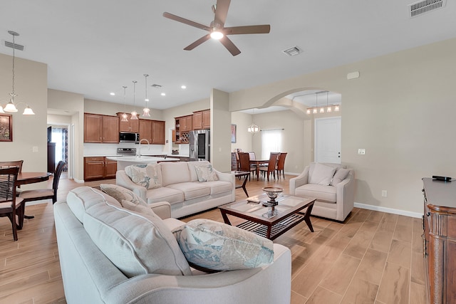 living room with light wood-type flooring, ceiling fan with notable chandelier, and sink