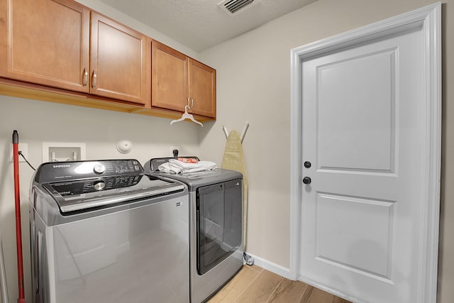 laundry area featuring light wood-type flooring, separate washer and dryer, and cabinets