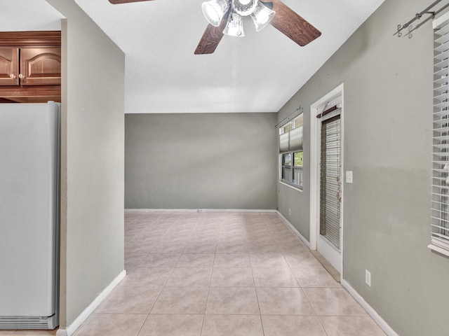 spare room featuring light tile patterned floors, ceiling fan, and baseboards