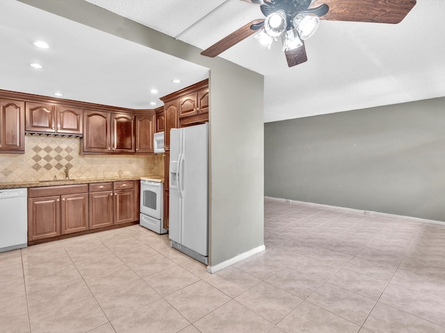 kitchen featuring backsplash, brown cabinetry, a sink, light stone countertops, and white appliances