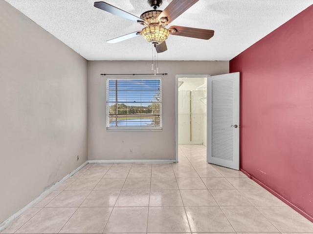 interior space with a textured ceiling, ceiling fan, light tile patterned flooring, and a spacious closet