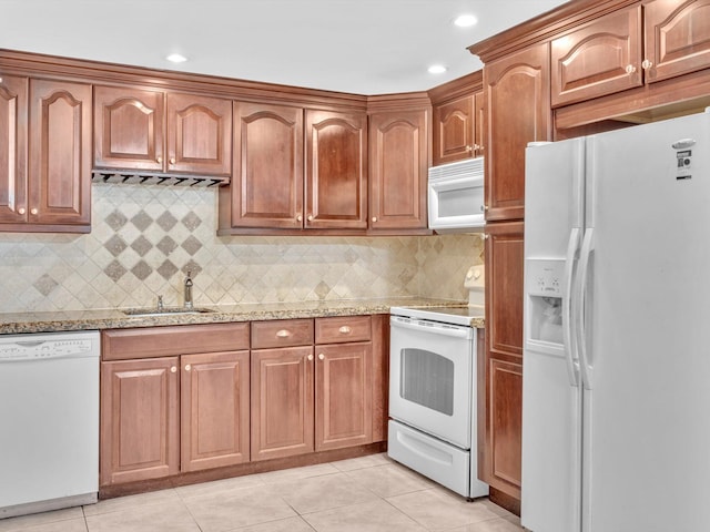 kitchen with light stone counters, brown cabinets, light tile patterned floors, a sink, and white appliances