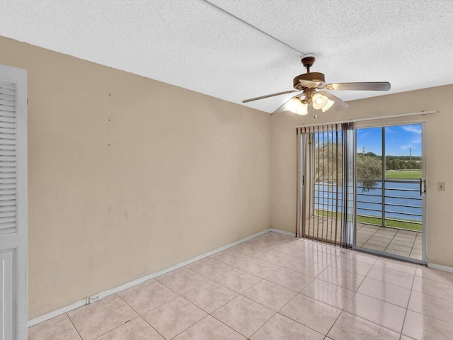 tiled spare room featuring a textured ceiling, ceiling fan, and a water view