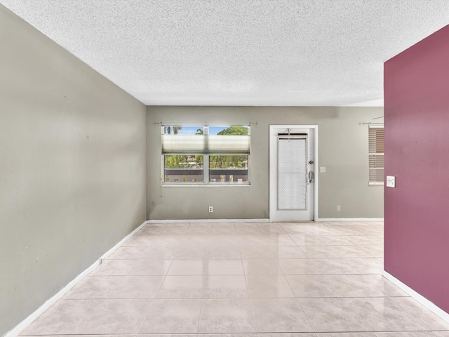 spare room featuring light tile patterned flooring, a textured ceiling, and baseboards