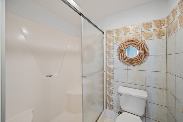 bathroom with toilet, an enclosed shower, and tile walls