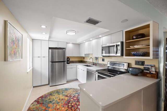 kitchen featuring a tray ceiling, appliances with stainless steel finishes, sink, kitchen peninsula, and light tile patterned flooring