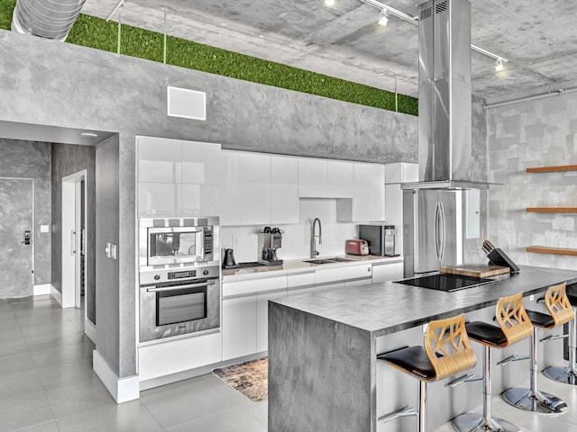 kitchen with island exhaust hood, stainless steel appliances, white cabinets, a sink, and modern cabinets