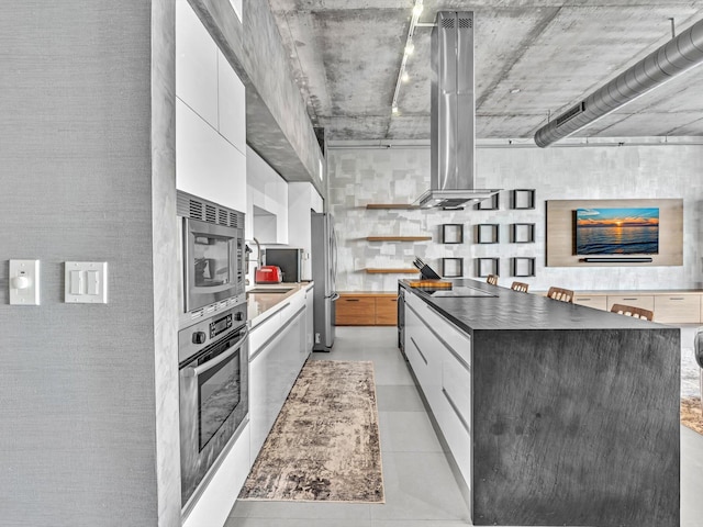 kitchen featuring stainless steel appliances, dark countertops, white cabinets, island range hood, and modern cabinets