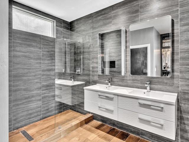 bathroom with a walk in shower, double vanity, a sink, and tile walls