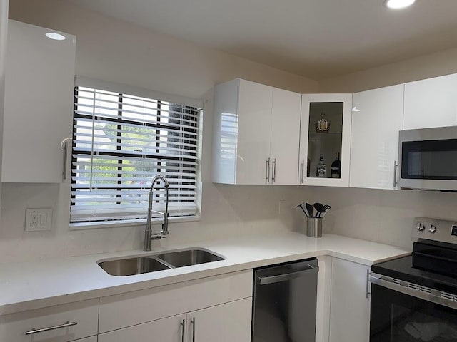 kitchen with a sink, white cabinets, light countertops, appliances with stainless steel finishes, and glass insert cabinets