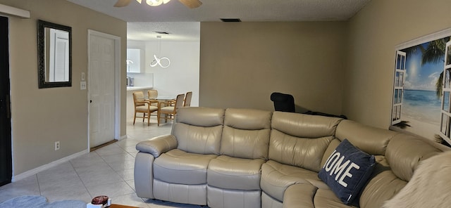 living area featuring a textured ceiling, light tile patterned flooring, visible vents, baseboards, and a ceiling fan