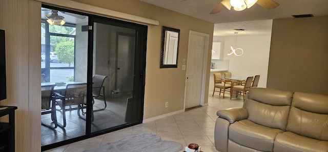 living area featuring light tile patterned flooring, ceiling fan, visible vents, and baseboards