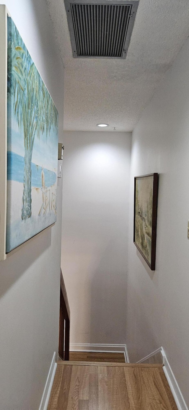 hall featuring a textured ceiling, wood finished floors, visible vents, and baseboards