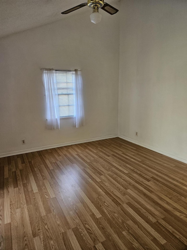 empty room featuring dark wood-style floors, vaulted ceiling, baseboards, and a ceiling fan