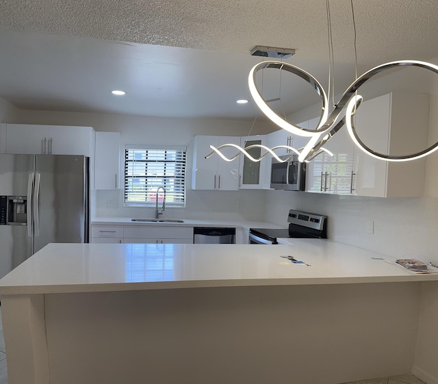 kitchen with a textured ceiling, a peninsula, a sink, light countertops, and appliances with stainless steel finishes