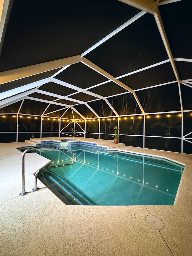 pool at night with glass enclosure and a patio area