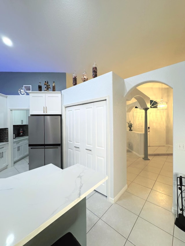 kitchen with stainless steel fridge, white cabinets, light tile patterned floors, and tasteful backsplash