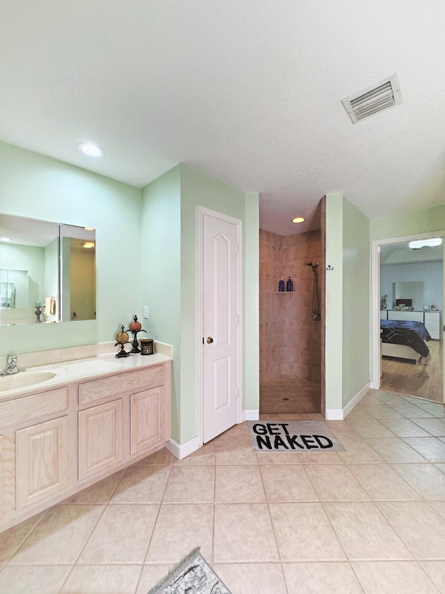 bathroom featuring tile patterned flooring, a tile shower, and vanity