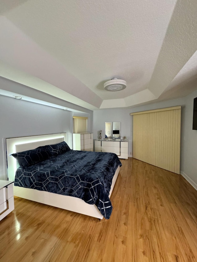 bedroom featuring light hardwood / wood-style flooring, a textured ceiling, and a tray ceiling