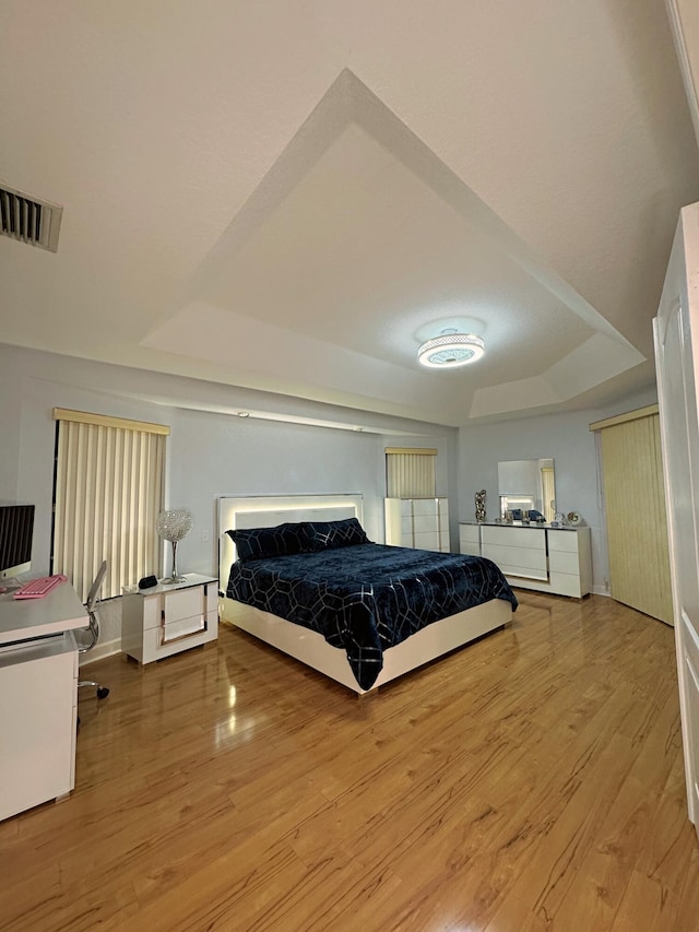 bedroom with light hardwood / wood-style flooring and a raised ceiling