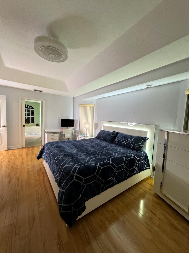 bedroom with light hardwood / wood-style flooring and a tray ceiling