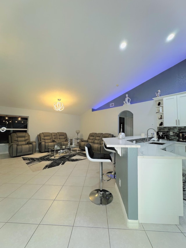 kitchen with decorative backsplash, a kitchen bar, white cabinetry, light tile patterned floors, and lofted ceiling