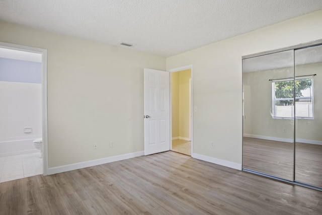 unfurnished bedroom featuring a textured ceiling, light wood-type flooring, ensuite bathroom, and a closet