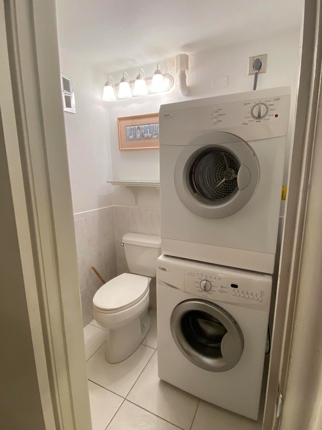 clothes washing area featuring tile walls, stacked washing maching and dryer, and light tile patterned floors