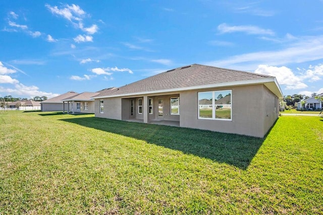 rear view of property with a shingled roof, a lawn, and stucco siding