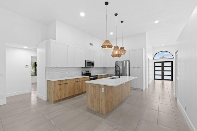 kitchen with a center island with sink, stainless steel appliances, light countertops, backsplash, and modern cabinets