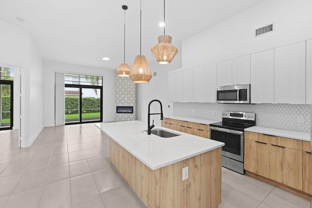 kitchen featuring appliances with stainless steel finishes, white cabinetry, tasteful backsplash, sink, and a center island with sink