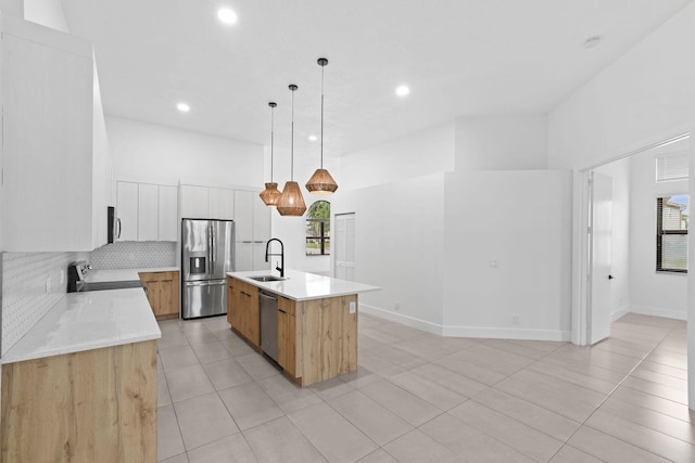 kitchen featuring backsplash, sink, appliances with stainless steel finishes, a center island with sink, and white cabinets