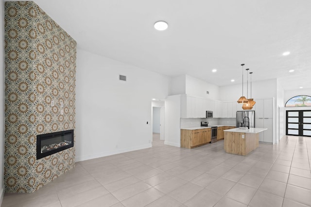 kitchen with a fireplace, appliances with stainless steel finishes, a kitchen island with sink, pendant lighting, and white cabinets