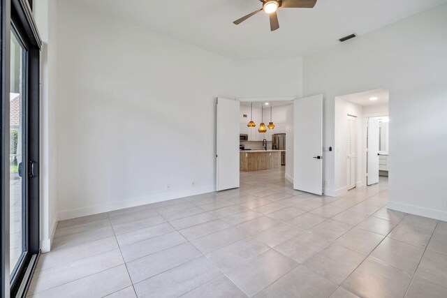 tiled empty room with ceiling fan, a high ceiling, and a healthy amount of sunlight