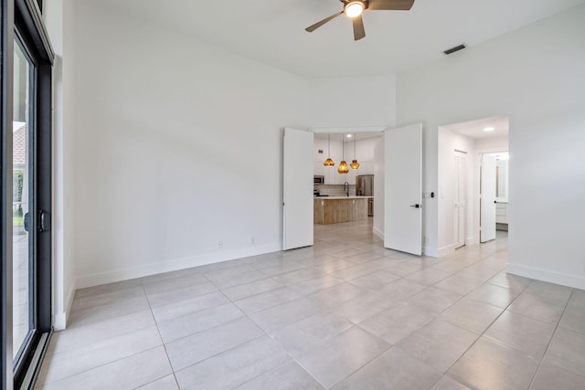 empty room featuring light tile patterned floors, baseboards, visible vents, and a ceiling fan