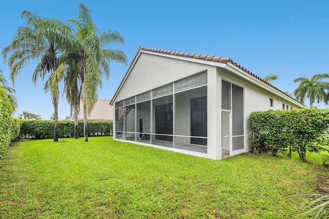 rear view of property featuring a tile roof, stucco siding, a lawn, a sunroom, and fence