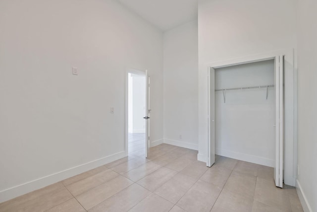 unfurnished bedroom featuring light tile patterned floors, a closet, a towering ceiling, and baseboards