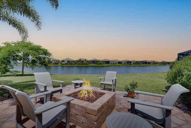 patio terrace at dusk featuring a yard, an outdoor fire pit, and a water view