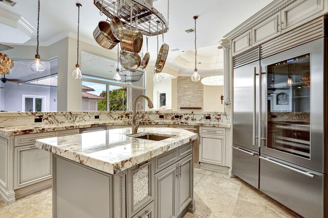 kitchen featuring backsplash, sink, an island with sink, hanging light fixtures, and built in fridge