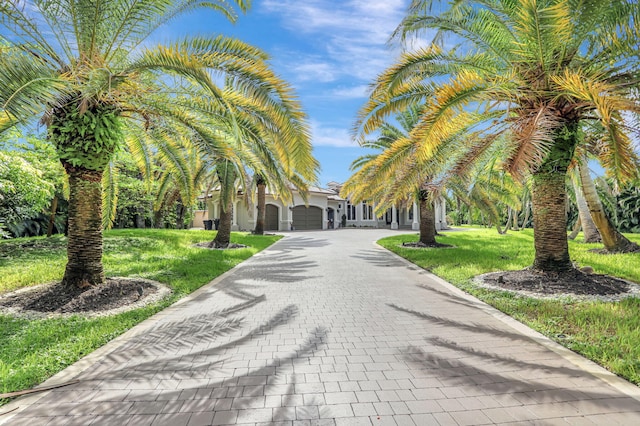 view of property's community with decorative driveway, an attached garage, and a lawn