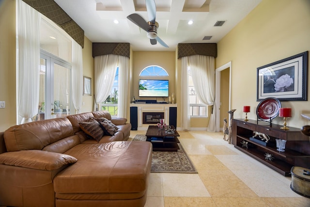 living room with coffered ceiling, a towering ceiling, beam ceiling, ceiling fan, and french doors