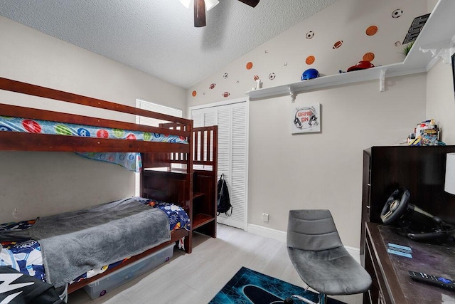 bedroom with a textured ceiling, vaulted ceiling, ceiling fan, light hardwood / wood-style flooring, and a closet