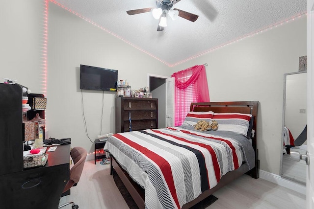 bedroom featuring ceiling fan, light wood-type flooring, lofted ceiling, and a textured ceiling