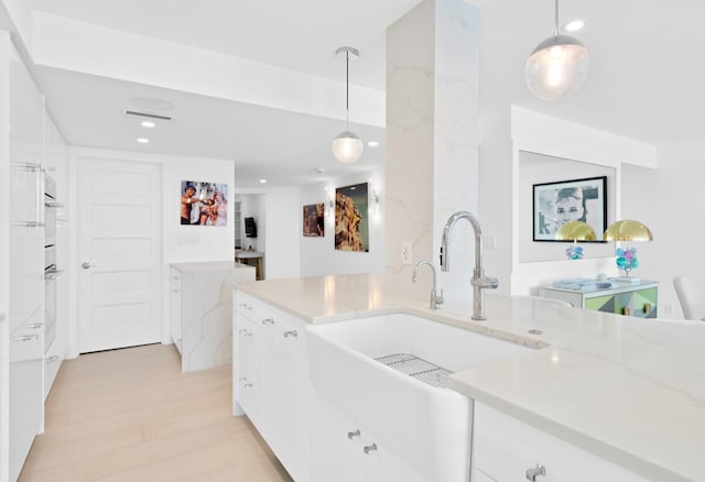 kitchen with light stone countertops, sink, hanging light fixtures, white cabinets, and light hardwood / wood-style flooring