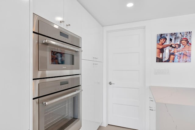 kitchen with light stone countertops, double oven, and white cabinetry