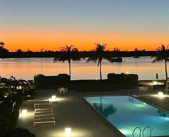 pool at dusk with a patio area and a water view