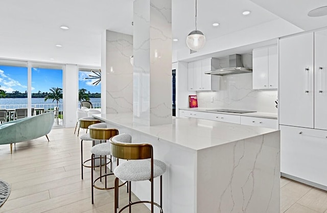 kitchen with white cabinets, a water view, wall chimney exhaust hood, and hanging light fixtures